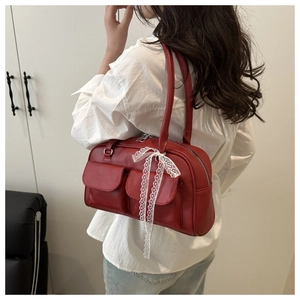 Detail view of red leather shoulder bag with flap pockets and white lace bows on model