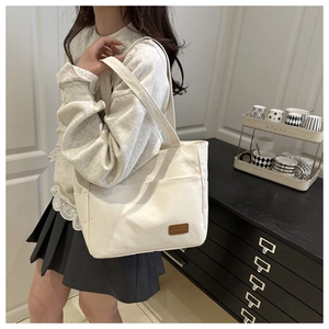 Detail of minimalist canvas tote bag showing faux leather patch and wide shoulder strap
