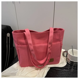 Close-up of pink canvas tote bag showing side pocket and leather logo brand tag