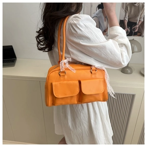 Close-up of bright orange shoulder bag with two front pockets and white lace bow detail