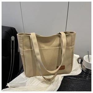 Detailed close-up of beige canvas tote bag with front pocket and leather logo patch