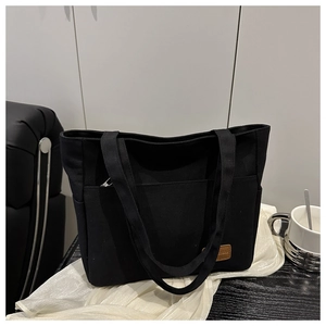 Detail view of black canvas tote bag showing wide strap and leather label detail