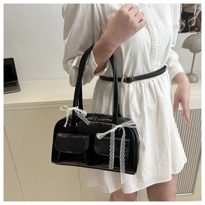 Detail of black faux leather handbag featuring white lace bow and front utility pockets