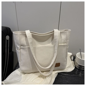 Detail of white canvas tote showing side pocket and brown leather logo on premium fabric