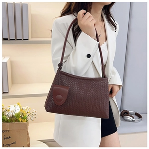 Close-up of brown woven leather shoulder bag with decorative round tag for women