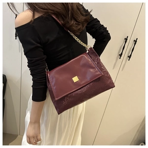 Close-up of wine red crossbody bag with golden square lock and elegant metal chain strap