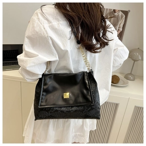 Detail of black faux snake pattern handbag with elegant gold square metal buckle clasp