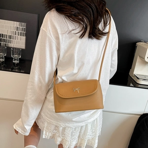 Petit sac bandoulière marron avec nœud argenté porté sur une robe blanche chic