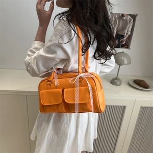 Bright orange multi-pocket handbag with lace bows worn as a trendy shoulder bag