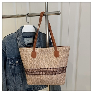 Detail of woven straw tote bag with brown faux leather handles and hollowed-out lace trim