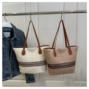 Detail of woven straw tote bag featuring black lace trim and brown leather handles