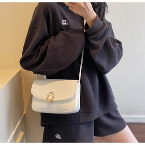 Detailed view of white minimalist crossbody bag with gold horseshoe buckle on model