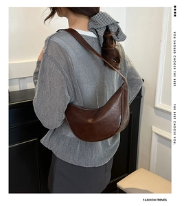 Side view of dark brown crescent shoulder bag shown on a model in a minimal setting