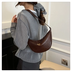 Detail of dark brown crescent shoulder bag with glossy finish on a female model