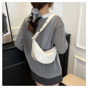 Detail of white half-moon bag with adjustable eyelet strap on model in modern room