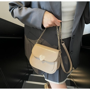 Detail of beige faux leather saddle bag featuring a gold heart-shaped metallic clasp