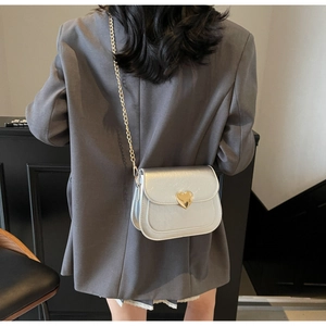 Close-up of silver patent leather saddle bag with gold heart clasp and chain strap