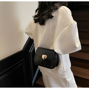 Detail of a chic black flap bag with a golden heart lock and chain strap on a model