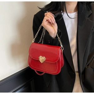 Detail of red glossy saddle bag featuring a heart-shaped metal buckle and gold chain strap