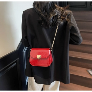 Close-up of bright red patent leather saddle bag with gold heart lock and chain strap