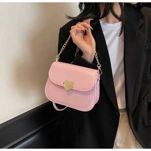 Detail of pink crossbody saddle bag featuring gold heart-shaped buckle and metal chain strap