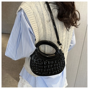 Detail of black patent leather handbag with circular handle and woven texture texture