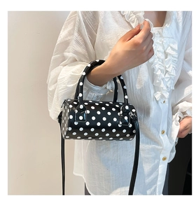 Close-up of black and white polka dot barrel bag with top handles and shoulder strap
