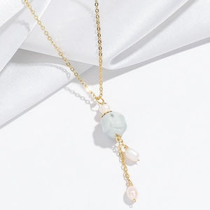 Détail d'un collier doré avec perle de jade verte et perles blanches sur soie blanche