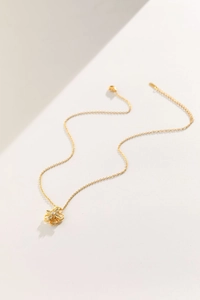 Dettaglio di una collana a quadrifoglio dorata rotante con micro-cristalli su fondo avorio