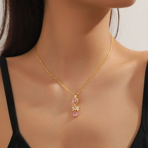 Detail of gold necklace with pink heart, bow charm and teardrop stone on model
