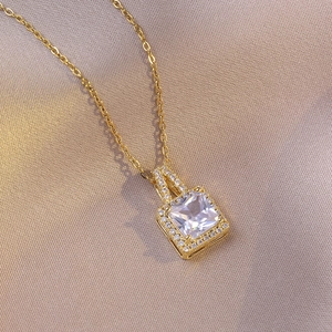 Elegant gold-tone necklace featuring a square-cut white zircon pendant on champagne satin