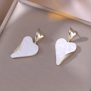 Close-up of gold-plated heart earrings with white mother of pearl inlay on jewelry pad
