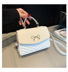 Detailansicht der weißen Handtasche mit beigem Stoffdeckel und goldener Schleifenschnalle