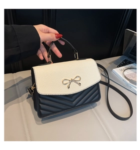Detail der Umhängetasche mit schwarzem Leder, cremefarbener Steppung und Schleife