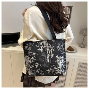 Close-up of black canvas tote bag featuring white bamboo print in a minimalist office setting