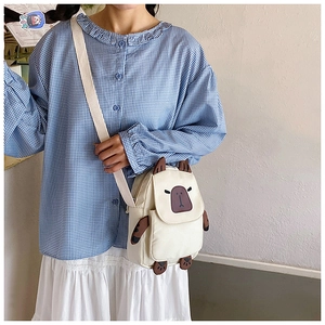 Detail of cute capybara cartoon crossbody bag in cream white canvas worn by model
