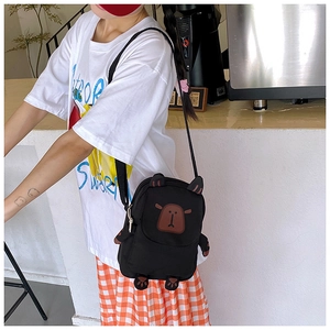 Detail view of a black canvas crossbody bag featuring a cute cartoon capybara on a model