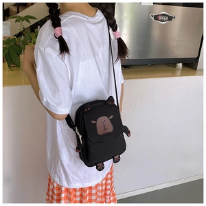 Detail view of the black cartoon capybara crossbody bag shown in a lifestyle cafe setting