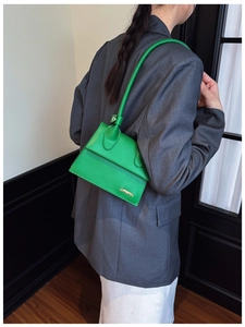 Close-up of bright green leather handbag with gold logo and long handles on a model