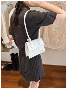 Detail of a white minimalist shoulder bag with gold hardware shown on a model