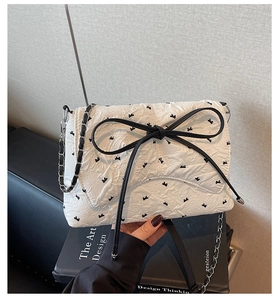 Detail of white textured shoulder bag with black bows and metallic chain strap