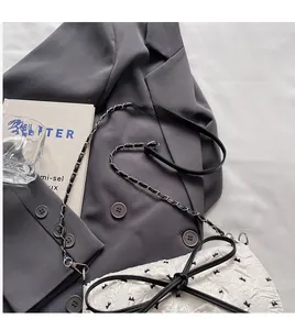 Detail of white bubble gauze bag featuring a black leather bow and silver chain strap
