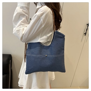 Detail of blue denim tote bag featuring white stitching pocket and brown braided rope strap