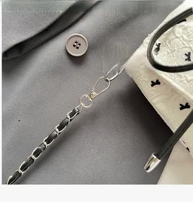 Detail of silver metal chain strap with black leather weave on white textured bag