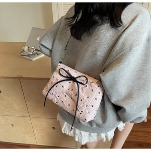 Detail of pink quilted crossbody bag featuring black bow patterns and chain strap