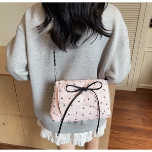 Pink quilted crossbody bag with black bow detail and woven chain strap shown on model