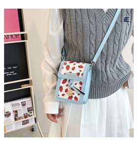 Detail view of light blue crossbody phone bag with strawberry print and gold hardware