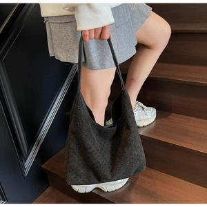Detail of a large black suede hobo bag with rhinestone studs worn by a model on stairs