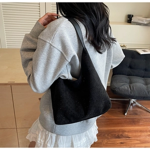Detail of a black hobo bag with subtle rhinestone studs and leather strap on a model