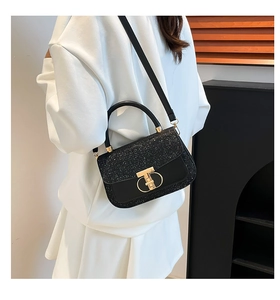 Chic black glitter crossbody bag with gold T-shaped buckle worn by a model in a modern room